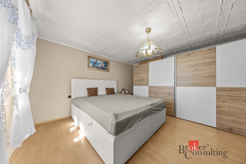 Bedroom in a family house with a bed, wardrobe, and wooden decor flooring.