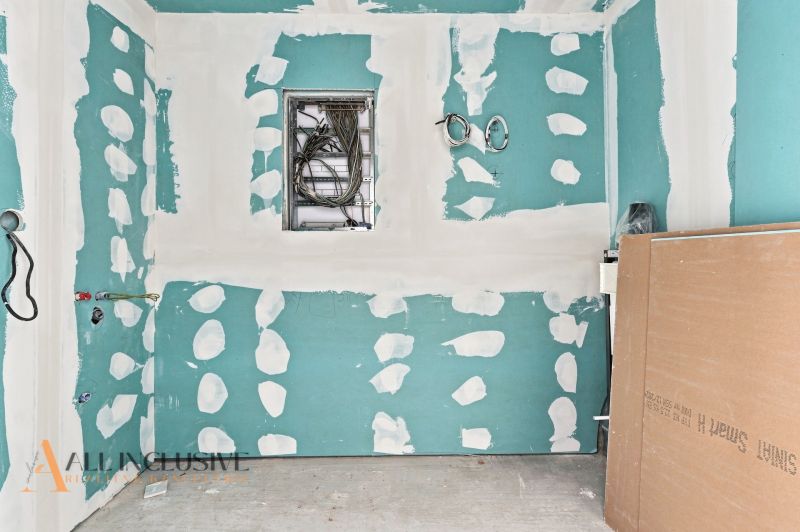 An unfinished room in a family house with exposed electrical wires and drywall.