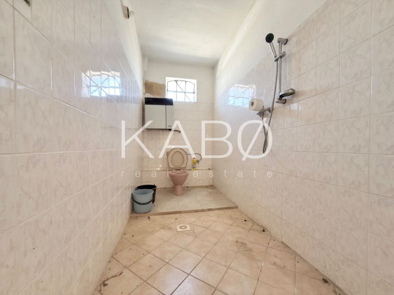 Bathroom with toilet, shower, and bucket, tiled walls, family house.