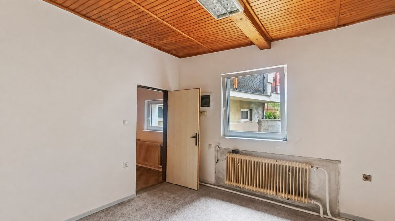 A room with white walls, a wooden ceiling, and a carpet in a family house.