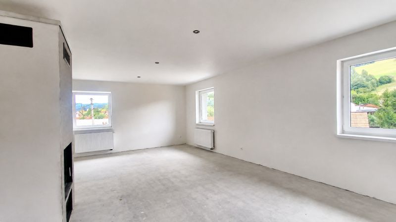 A spacious room in a family house with white walls and large windows.