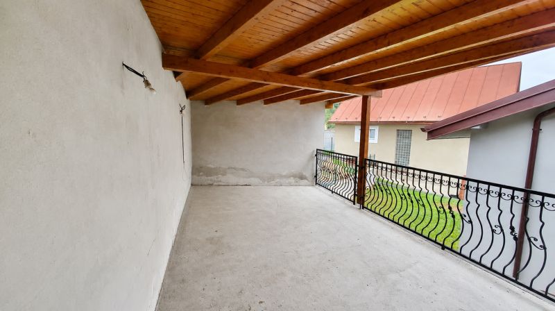 Covered terrace of a family house in Ochodnica with a wooden ceiling and wrought iron railing.