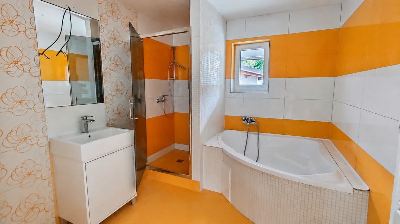 A bathroom with orange and white tiles, a bathtub, and a shower in a family house.