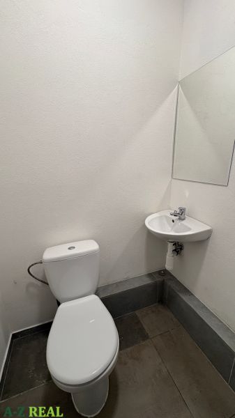 A restroom with a sink in commercial premises, white walls, dark tiles.