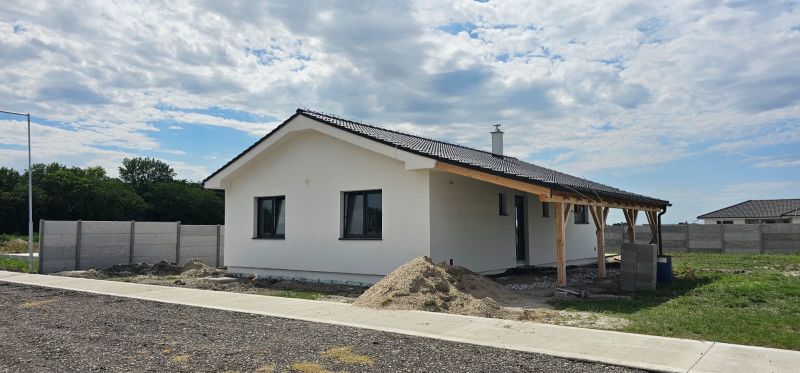 A family house in Bellova Ves with a white facade, a sloped roof, and surrounding buildings.