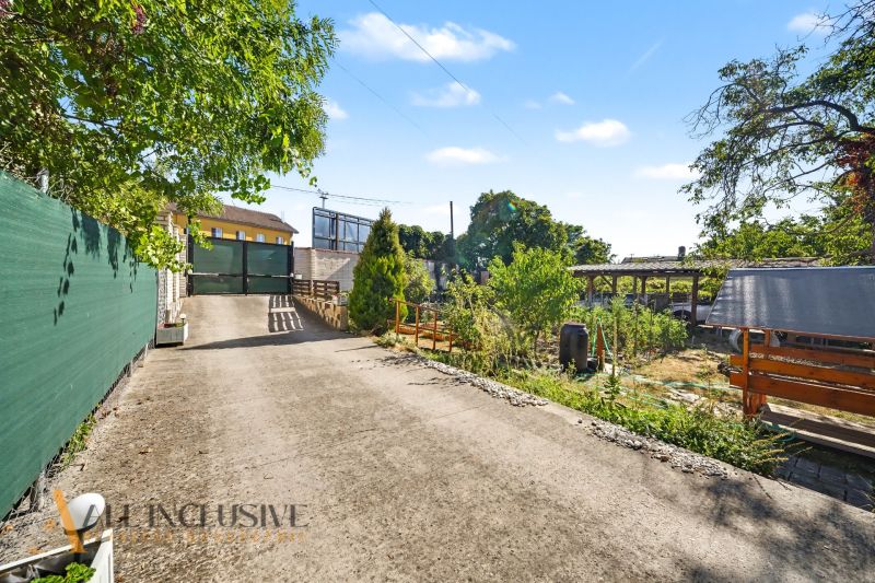 Access road to a residential plot in the town of Pezinok surrounded by greenery and a fence.