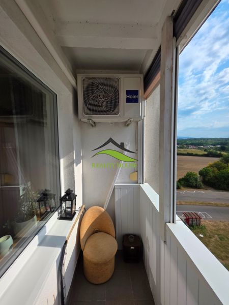 A narrow balcony in a 3-room apartment with a sofa and air conditioning, overlooking nature.