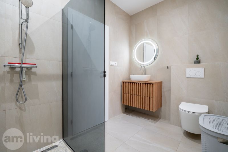 A bathroom in a family house with a sink, a shower, and a backlit mirror.