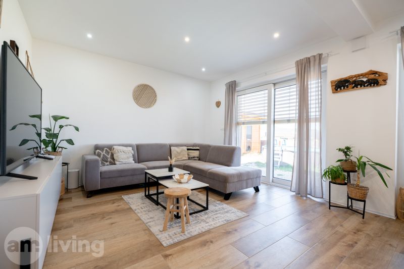 Living room in a family house with a gray sofa, wood-patterned flooring, and large windows.