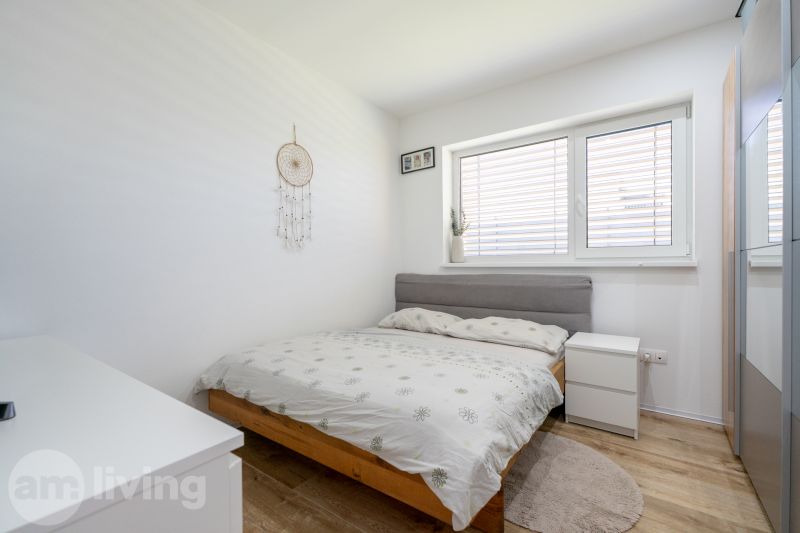 Bright bedroom with a bed, wood-patterned floor, and a dreamcatcher on the wall.