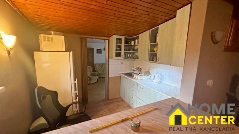 Interior of a cottage with a kitchen unit, refrigerator, and wooden decor flooring.