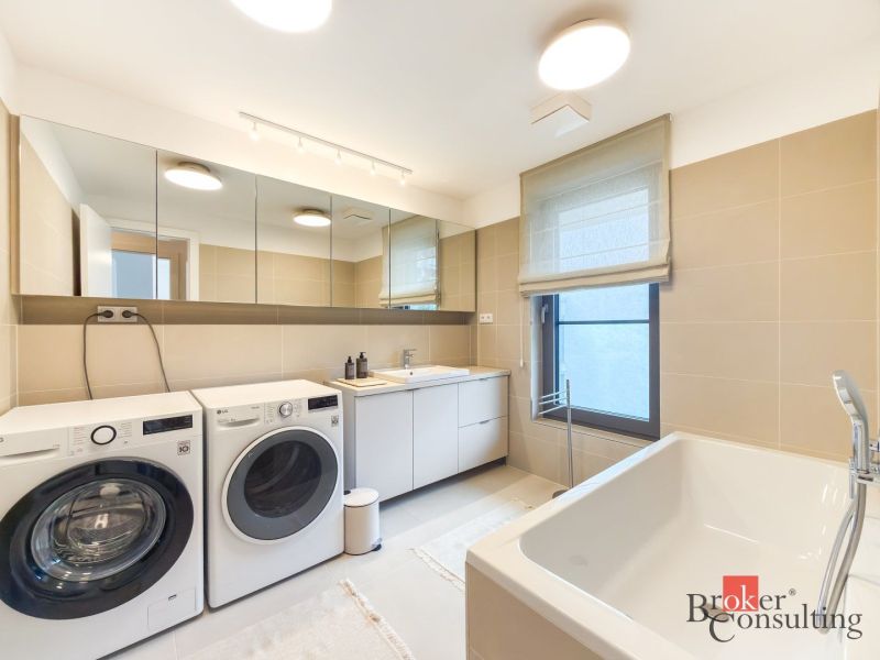 A bathroom in a 4-room apartment with a washing machine, dryer, bathtub, and mirror cabinet.
