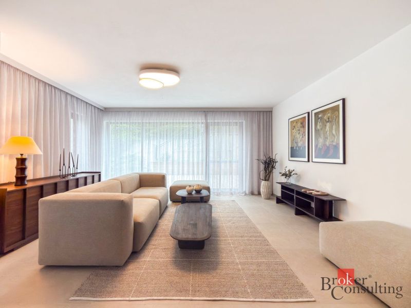 Living room in a 4-room apartment with a beige sofa, wooden cabinets, and large windows.