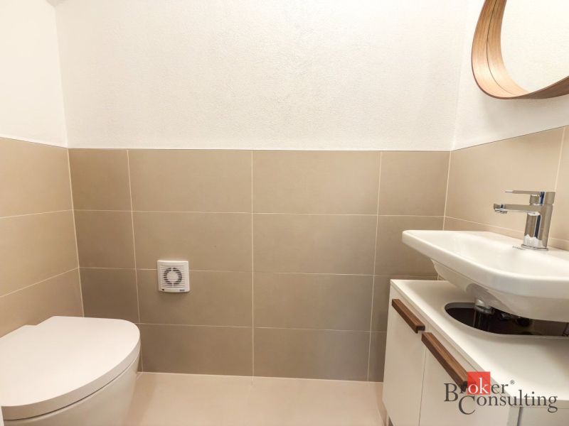 Bathroom with toilet, sink, mirror, and beige tiles in a 4-room apartment.