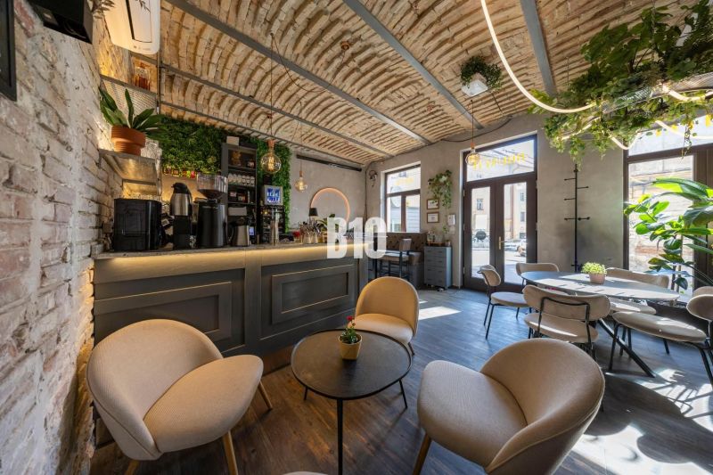 An interior with a bar surrounded by plants, a floor with a wooden decor, comfortable seating.