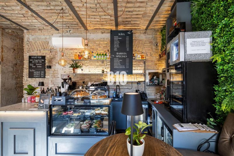 A café with brick walls, a counter with a menu of food and drinks, plants in the gastro area.