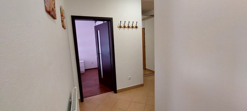 A hallway in a 3-room apartment with a coat rack wall and doors, with a view of the wood-patterned floor.