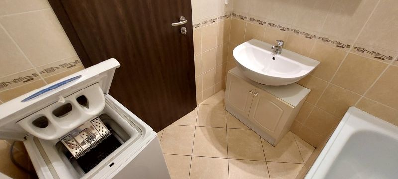 A bathroom with a washing machine, sink, and beige tiles in a 3-room apartment.