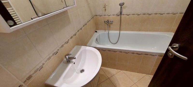 Bathroom with a bathtub and a sink in a 3-room apartment with light tiles.