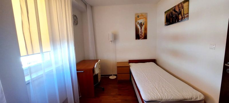 A room in a 3-room apartment with a wooden decor floor, a bed, and a table.