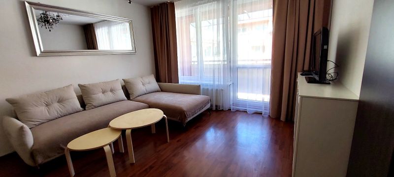 Living room with a sofa, mirror, television, and wooden decor flooring in a three-room apartment.