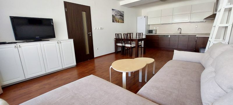 Living room of a three-room apartment with a wooden decor floor, kitchenette, and dining table.
