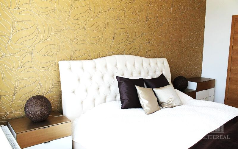A bedroom in a 3-room apartment with golden wallpaper and a white headboard.