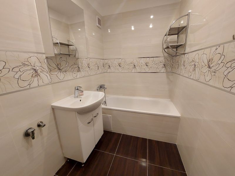 Bathroom in a 3-room apartment with a bathtub, decorative tiles, and a wooden decor floor.
