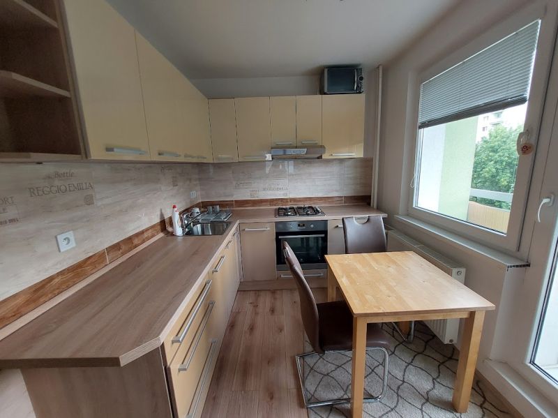 A kitchen in a 3-room apartment with a wooden decor floor and a balcony.