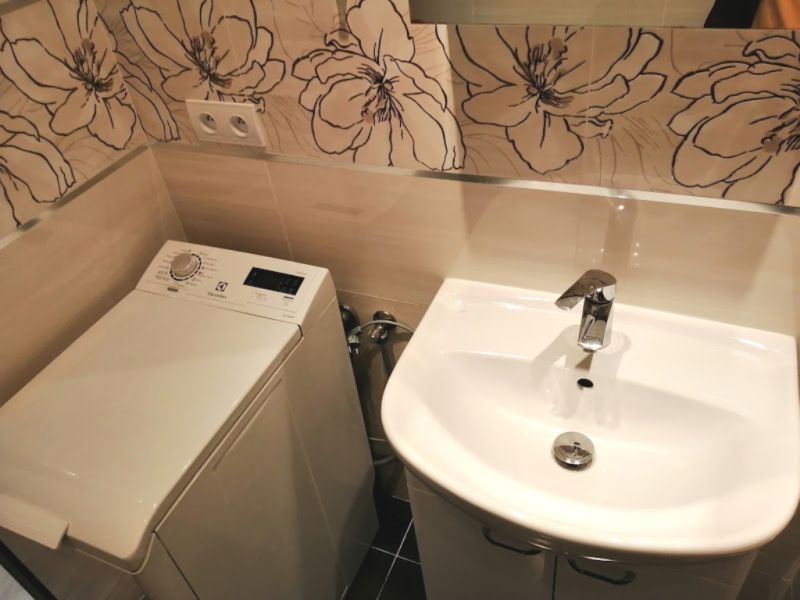 A bathroom in a 3-room apartment with a washing machine, a sink, and floral tiles on the wall.