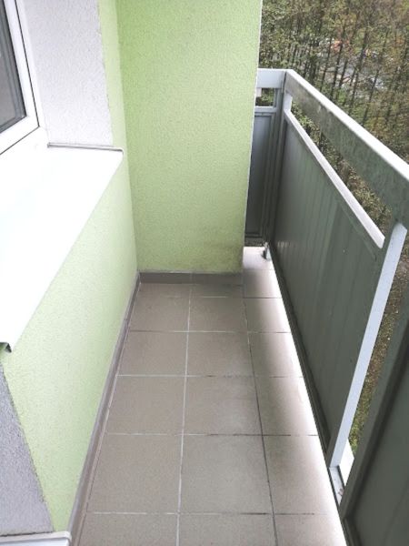 A balcony with tiles in a 3-room apartment with green walls and a view of the trees.