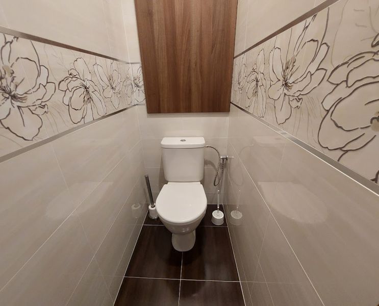 A toilet with floral tiles and a wooden decor floor in a 3-room apartment.