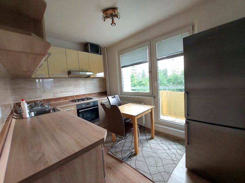A kitchen in a 3-room apartment with a wooden decor floor, light cabinets, and appliances.