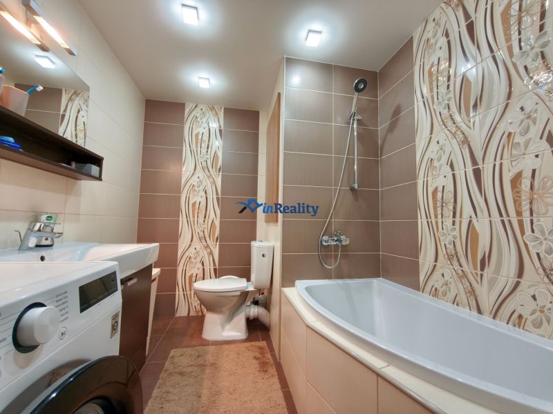 Bathroom in a 3-room apartment with a bathtub, washing machine, and brown tiles.