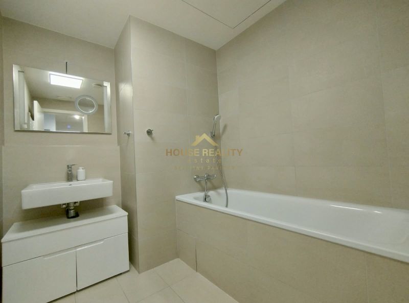 Bathroom with a bathtub and a sink in a 2-room apartment, beige tiles and a mirror.