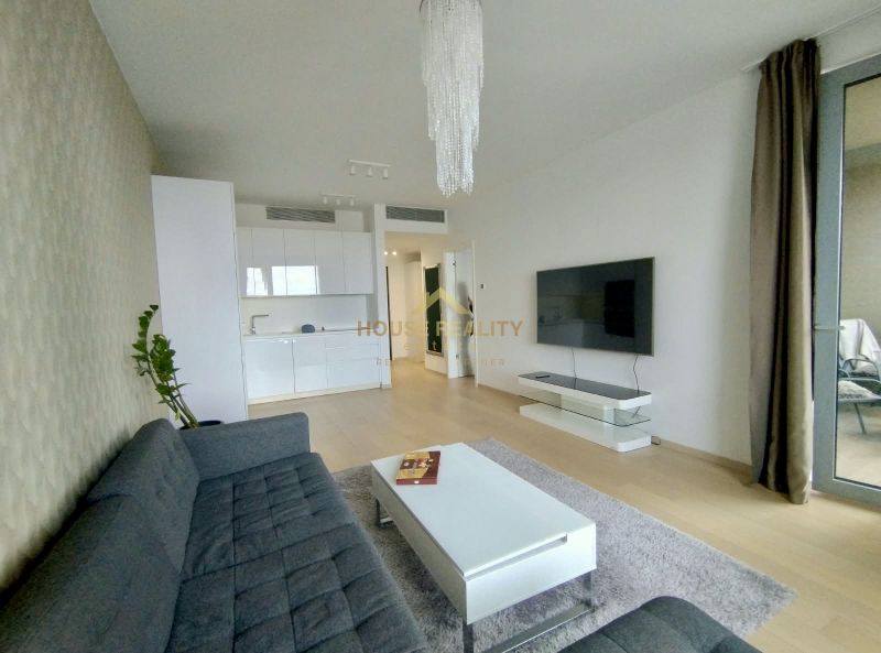 Living room in a two-room apartment with a wooden decor floor, a sofa, and a kitchen unit.