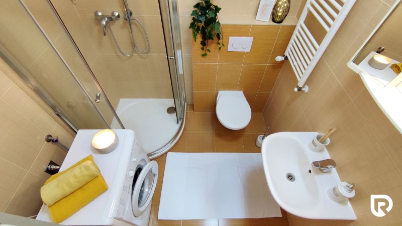 A bathroom in a 2-room apartment with a washing machine, shower, and toilet.