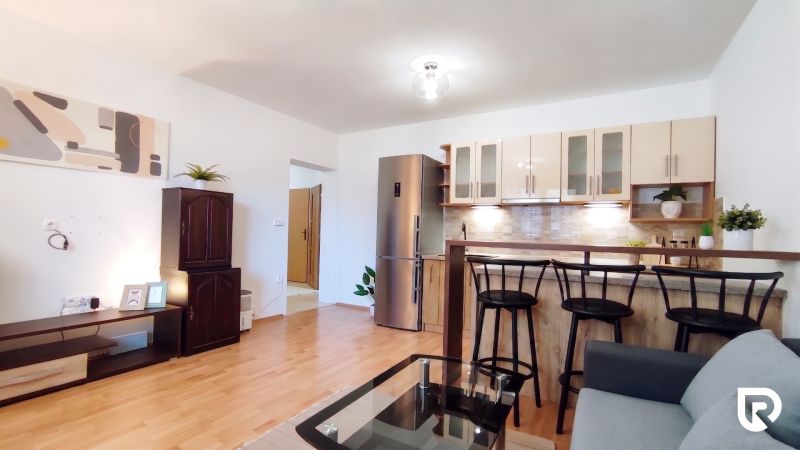 Living room with a kitchenette, glass table, and wooden decor flooring in a two-room apartment.