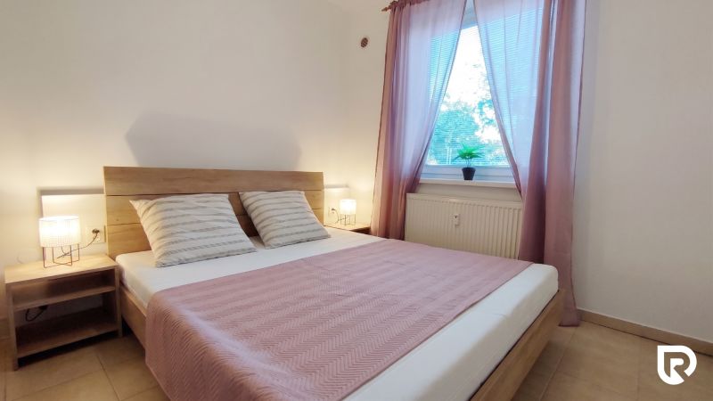 Bedroom in a two-room apartment with wooden decor, beige tiles, pastel textiles.