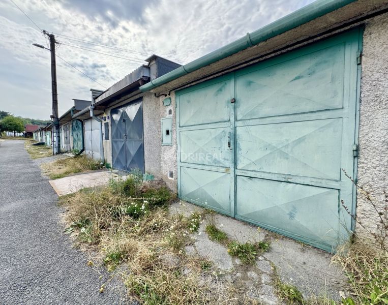 A row of garages in Detva with blue doors and neglected vegetation.