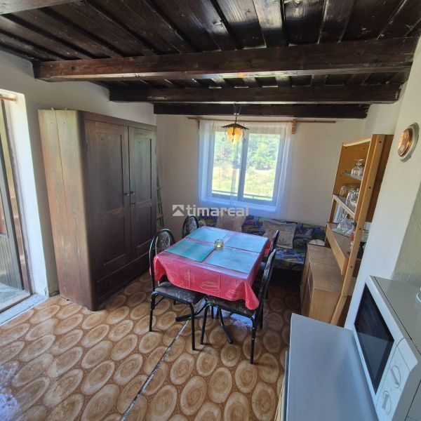 Dining room in a cottage with a round table, wooden decor flooring, view from the window.
