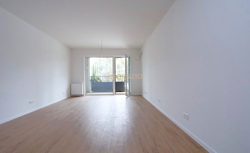 A spacious room with a wooden decor floor and balcony doors in a studio apartment.
