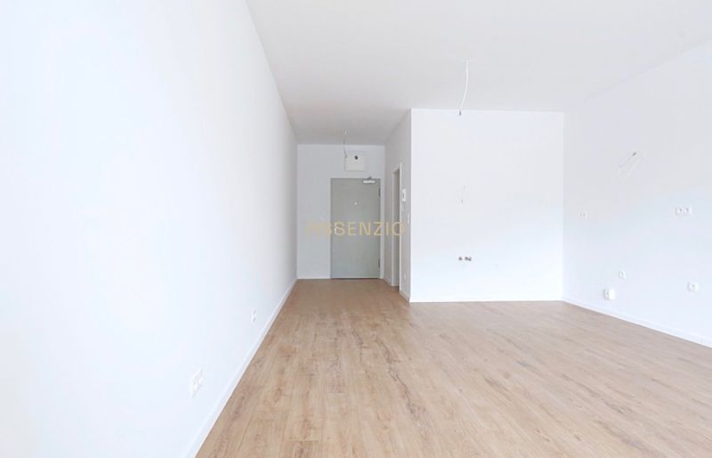 Interior of a 1-room apartment with a wooden decor floor and white walls.