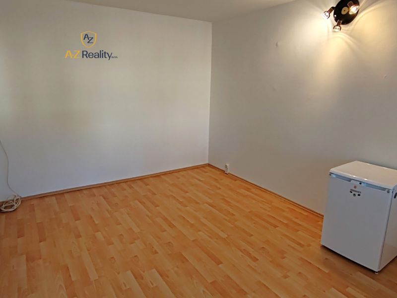 A studio apartment with a wooden floor, light-colored walls, and a small refrigerator.