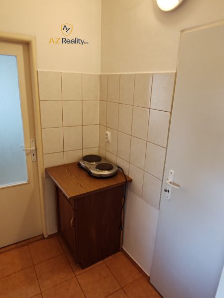 A kitchenette in a studio apartment with an electric stove and a cabinet, tiled.