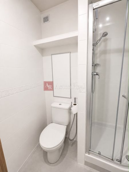 Bathroom in a 2-room apartment with a toilet and a shower, white tiles.