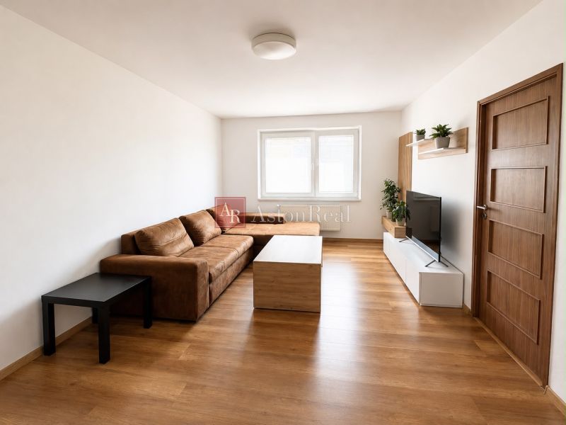 Living room in a two-room apartment with a sofa, television, and wooden decor flooring.