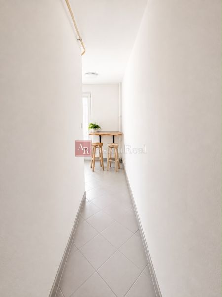 A narrow hallway in a 2-room apartment with tiles leading to a small table and chairs.