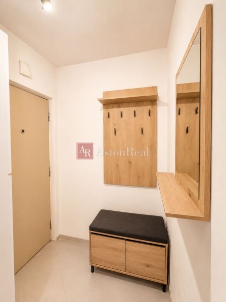 Hallway with a coat rack, mirror, and bench in a 2-room apartment, floor with wooden decor.