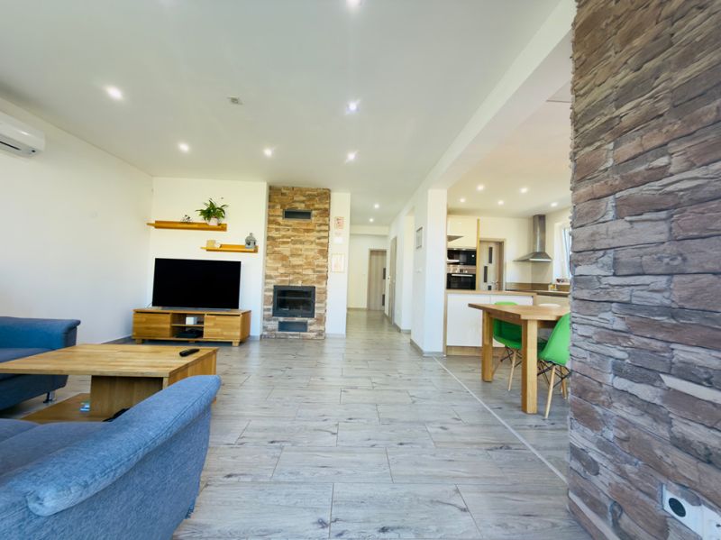 Living room with a fireplace, wooden decor flooring, and a kitchenette in a family house.